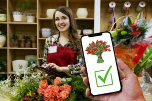A florist surrounded by flowers with a mobile phone displaying flowers and a check box.